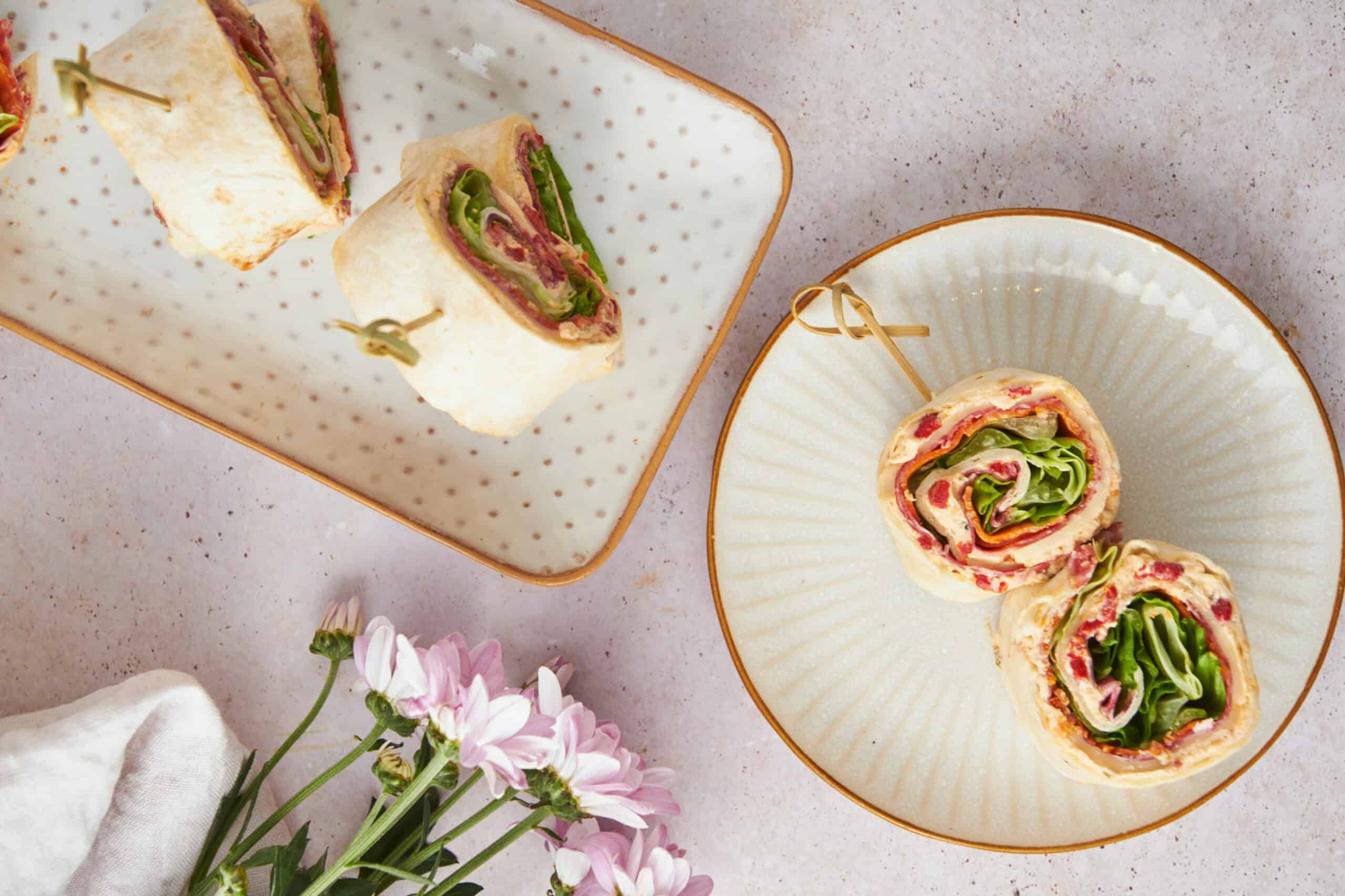 Fresh veggie pinwheel sandwiches on decorative plates, perfect for healthy snacks or parties. Colorful, creamy, and delicious, these roll-ups feature crisp lettuce, cold cuts, and cheese in a soft wrap.
