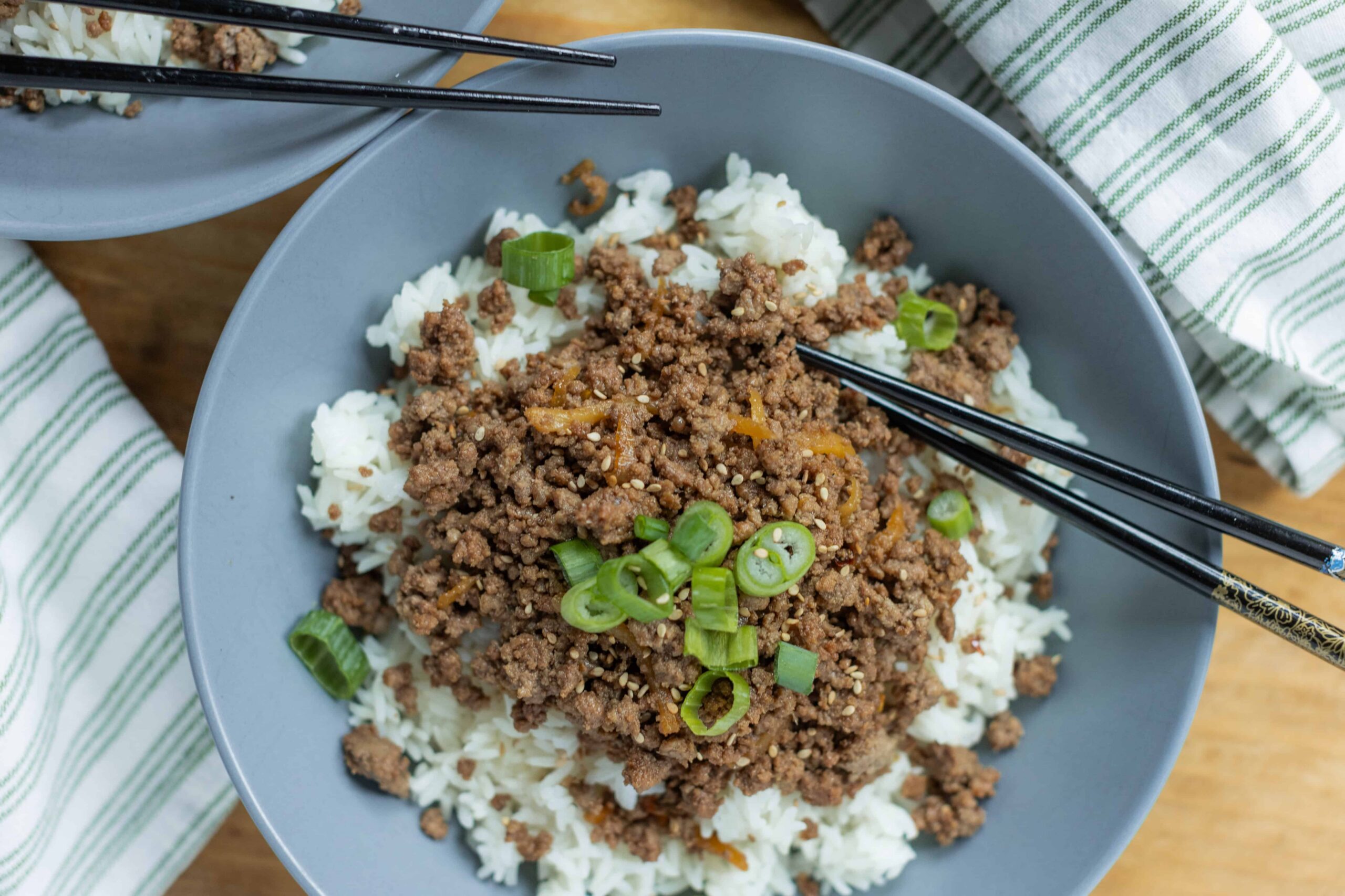 Minced beef stir-fry served over steamed white rice with chopped green onions on top, on a gray plate with black chopsticks, showcasing a delicious Asian-inspired meal for dinner or lunch.