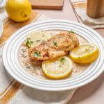 Juicy lemon grilled chicken breast served with lemon slices and fresh herbs on a white plate, perfect for healthy dinner recipes and citrus-flavored poultry dishes.