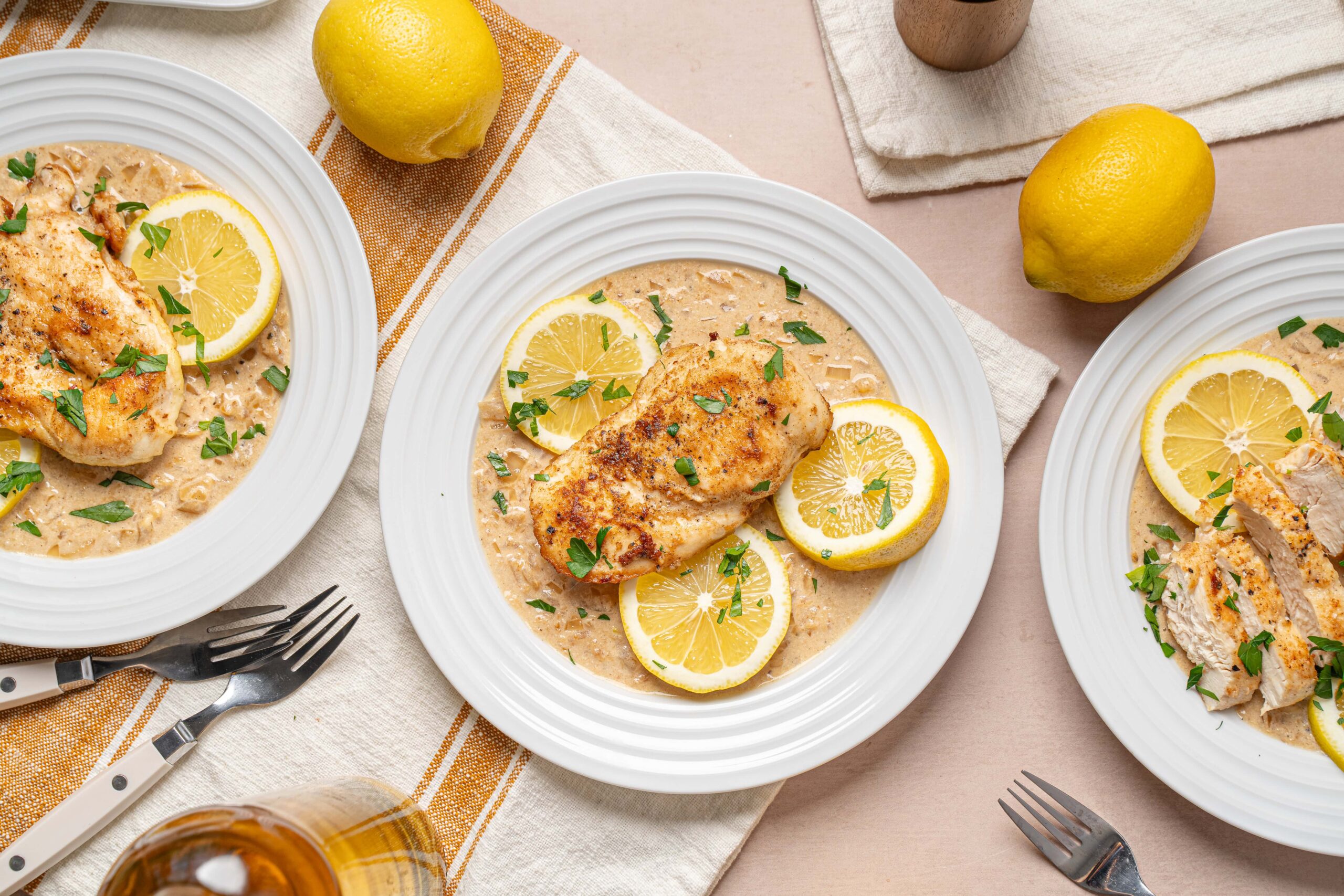 Juicy lemon herb chicken breast served with creamy lemon pasta on white plates, garnished with fresh parsley and lemon slices, perfect for easy summer dinner or lunch.