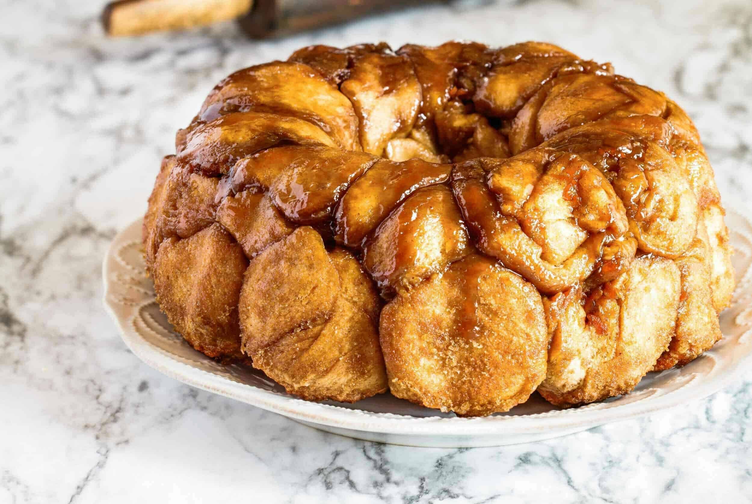 Butter roll baked bread pudding with caramel glaze on a decorative plate on marble surface.