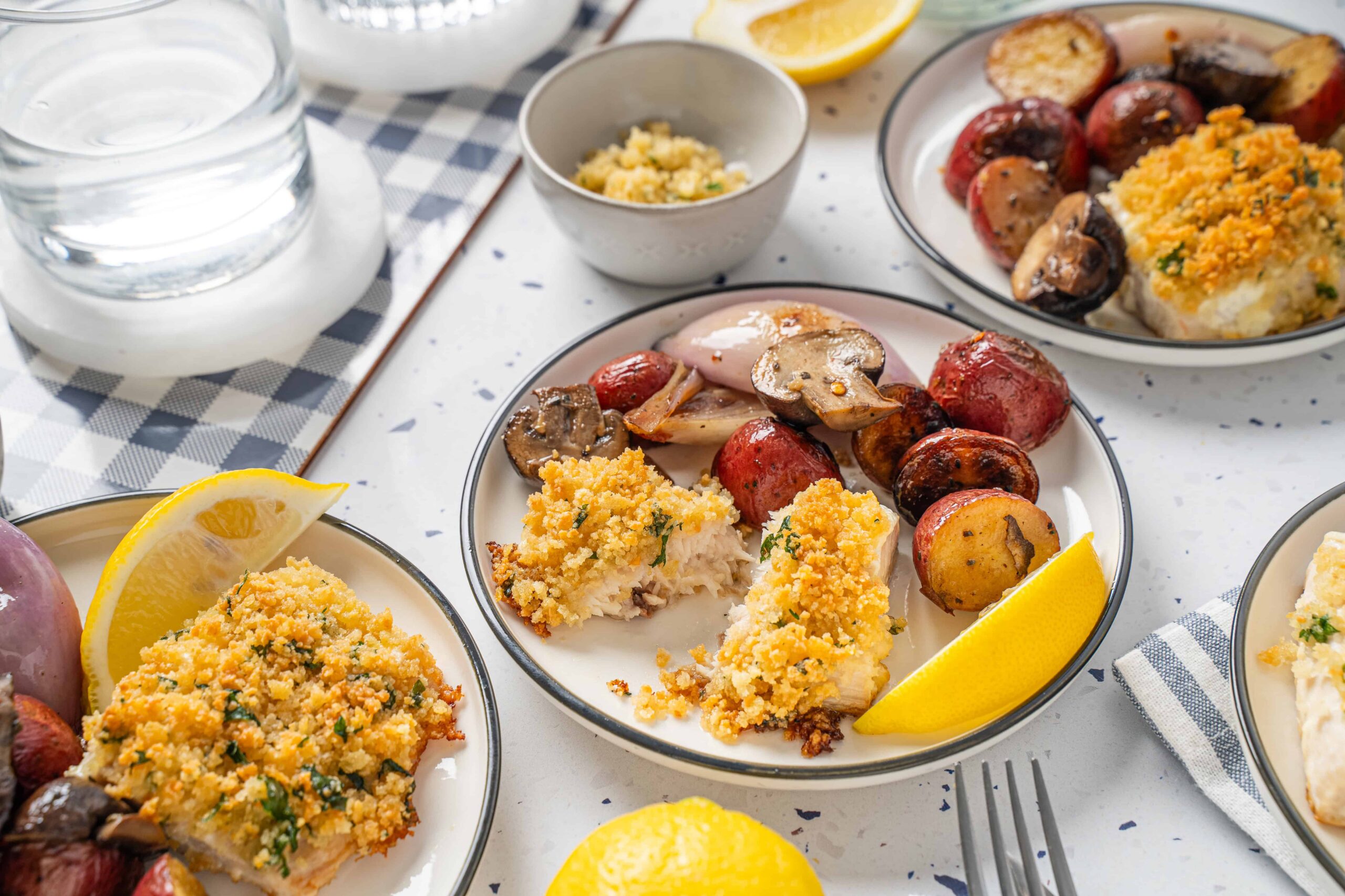 Golden baked fish fillets with crispy breadcrumb topping served with roasted new potatoes and grilled vegetables, garnished with lemon wedges for a delicious healthy seafood meal.