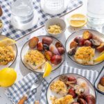 Succulent baked fish fillets topped with golden breadcrumbs, served with roasted red potatoes, onions, and mushrooms on a bright white speckled table, garnished with lemon wedges for a flavorful seafood meal.