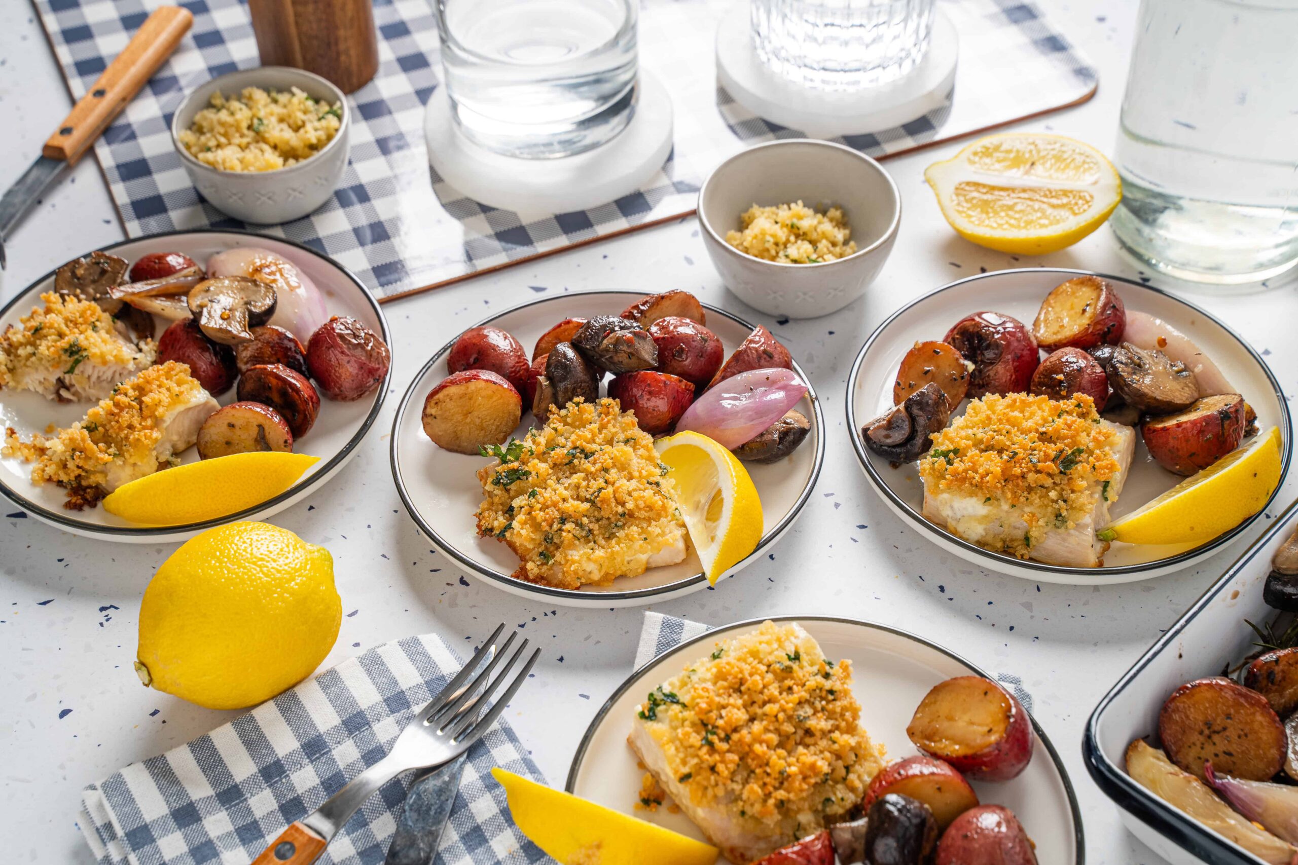 Succulent baked fish fillets topped with crispy breadcrumb crust, served with roasted baby potatoes and sautéed mushrooms, garnished with lemon wedges for a flavorful seafood dish.