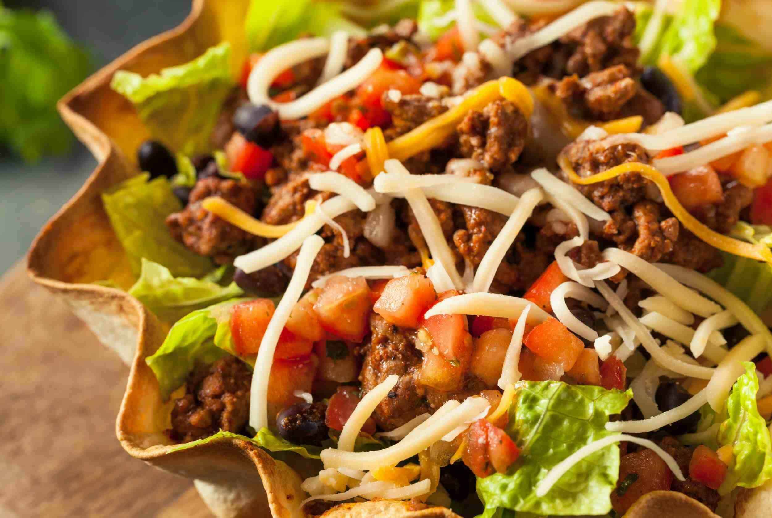 Fresh taco salad with seasoned ground beef, shredded cheese, beans, diced tomatoes, lettuce, and tortilla shell. Perfect for a quick and flavorful meal.
