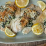 Succulent baked chicken breasts topped with spinach, cheese, and a lemon garnish on a white platter.