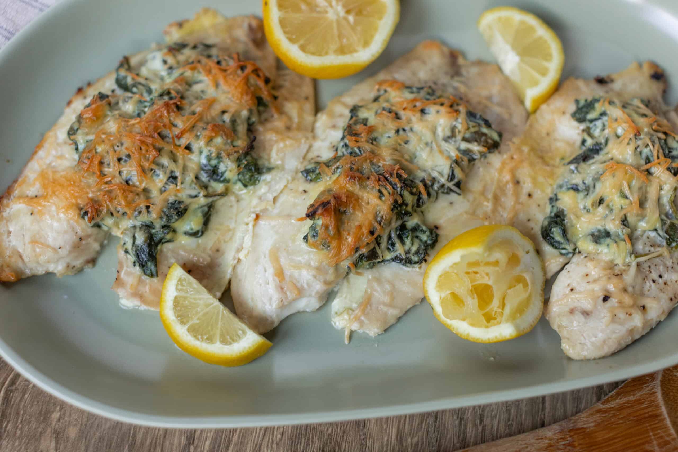 Succulent baked chicken breasts topped with spinach, cheese, and a lemon garnish on a white platter.