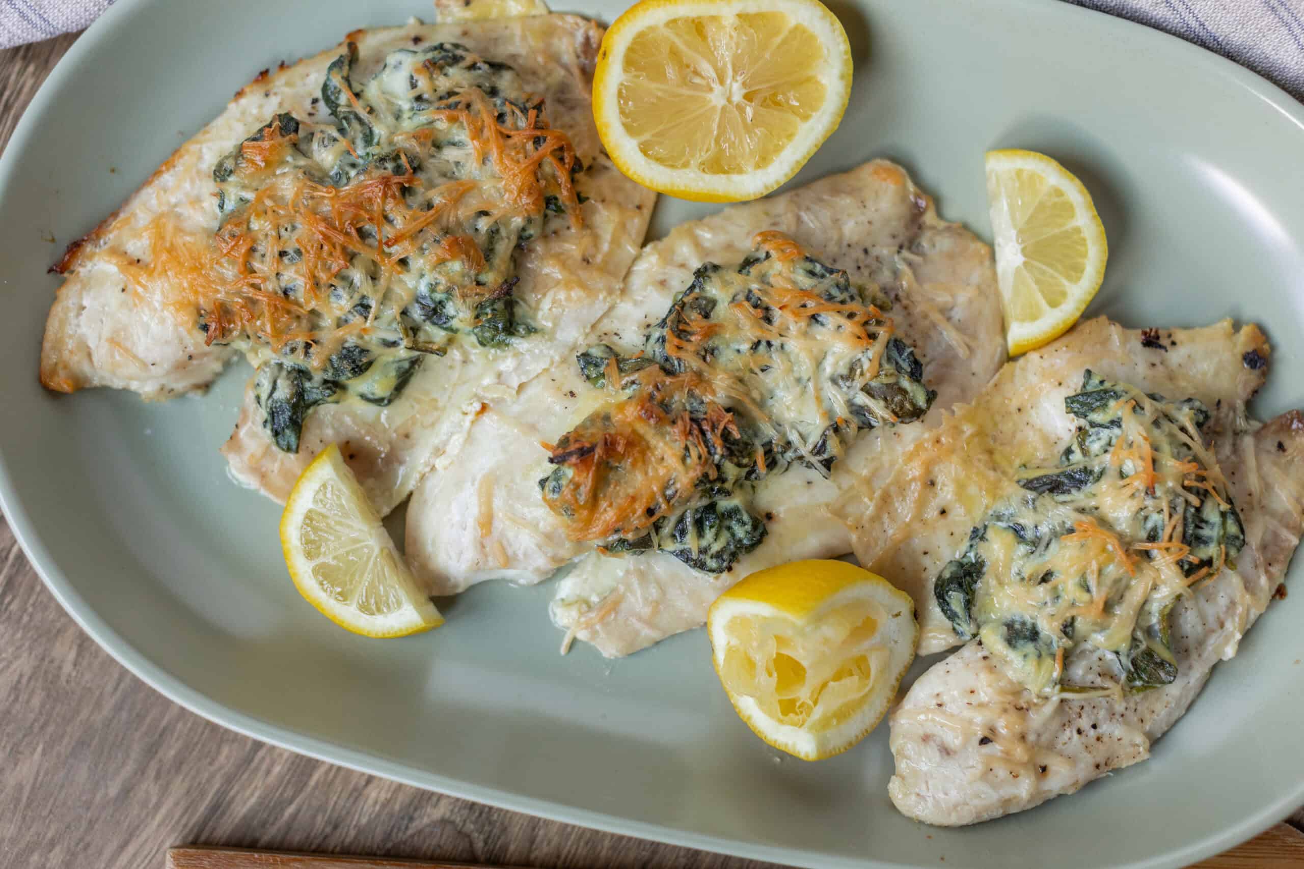 Baked chicken breasts topped with spinach, shredded carrots, and melted cheese served with lemon wedges for a nutritious and flavorful meal. Perfect for easy weeknight dinners or healthy family dishes.