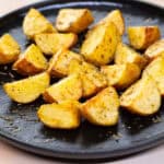 Crispy roasted potatoes seasoned with herbs on a black plate. Perfect side dish for breakfast, lunch, or dinner, showcasing golden-brown, flavorful, and delicious potato wedges. Ideal for healthy, easy recipes.