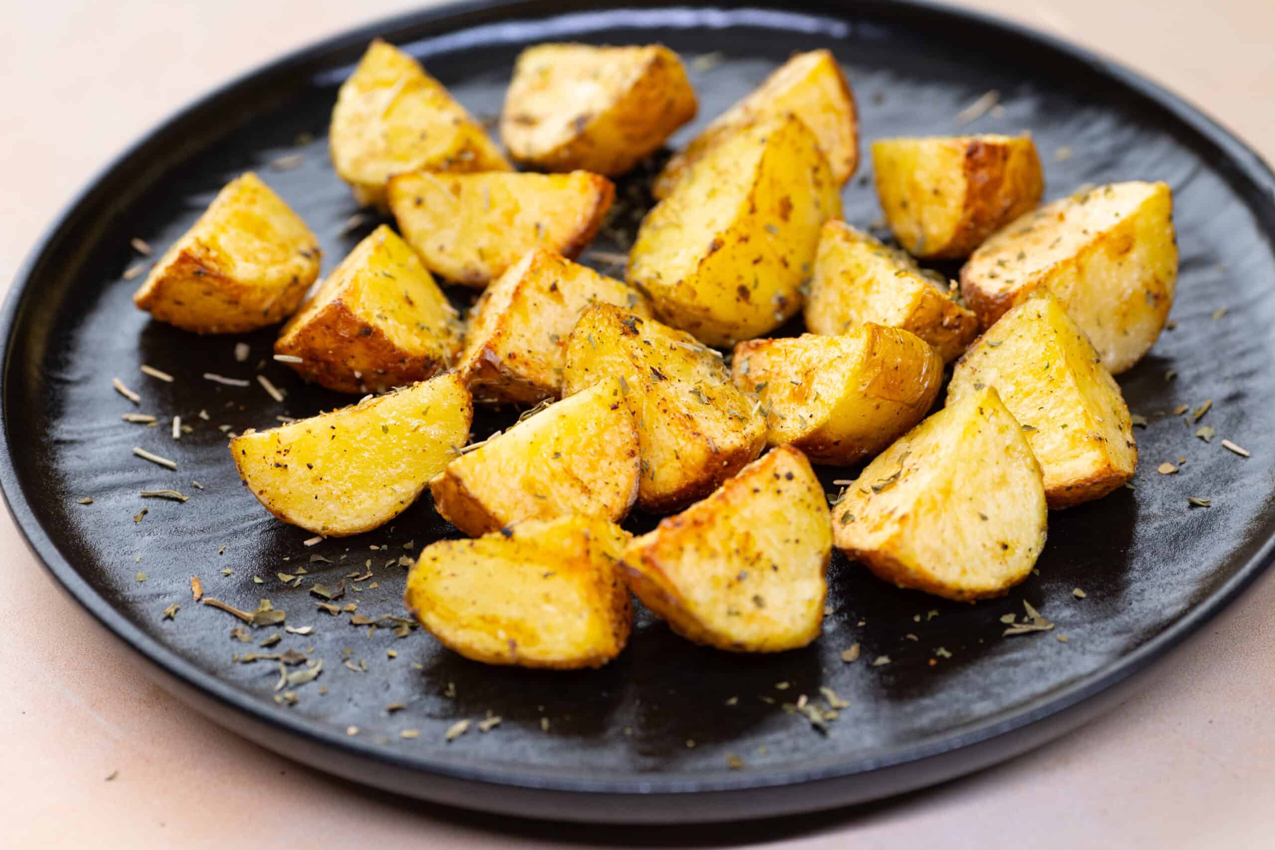 Crispy roasted potatoes seasoned with herbs on a black plate. Perfect side dish for breakfast, lunch, or dinner, showcasing golden-brown, flavorful, and delicious potato wedges. Ideal for healthy, easy recipes.