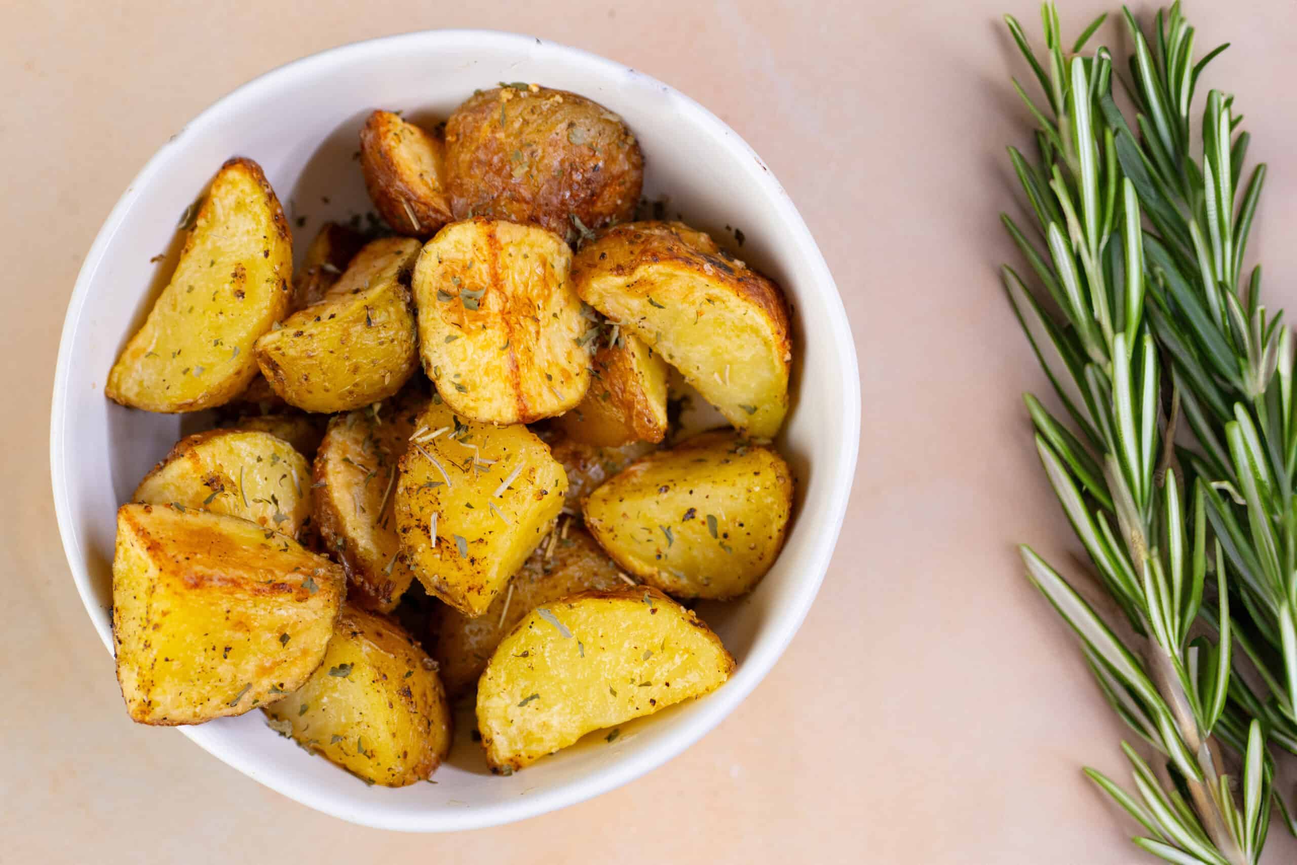 Crispy roasted potato wedges with herbs in a white bowl, served as a delicious side dish or snack. Perfect for breakfast, lunch, or dinner, seasoned with spices and herbs for flavor.