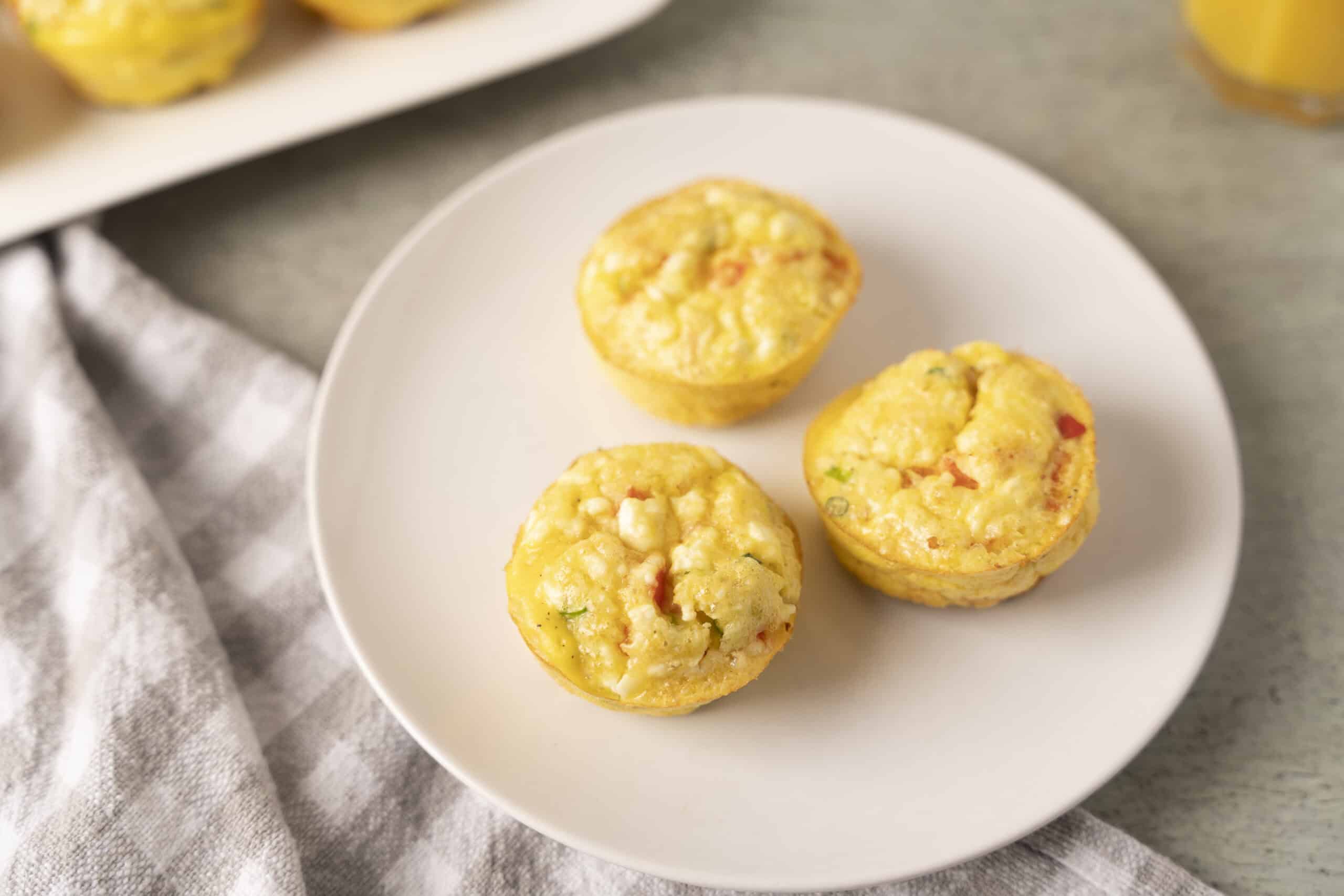 Fluffy savory egg muffins with colorful vegetables on a white plate, healthy breakfast idea.