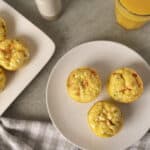 Fluffy baked egg muffins with cheese, vegetables, and ham on white plates, served as a healthy breakfast or snack option. Perfect for meal prep and easy to customize with favorite ingredients.