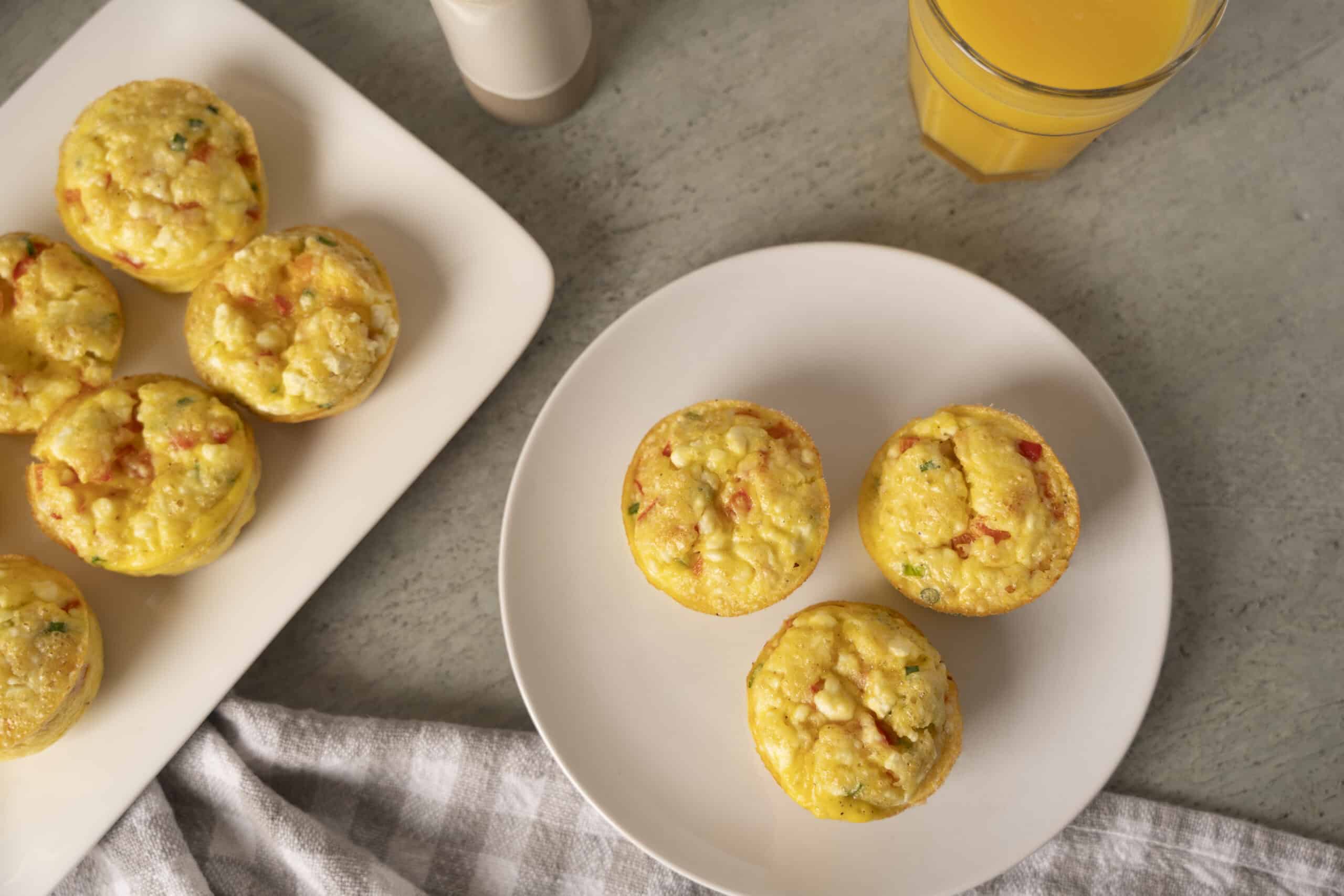 Fluffy baked egg muffins with cheese, vegetables, and ham on white plates, served as a healthy breakfast or snack option. Perfect for meal prep and easy to customize with favorite ingredients.