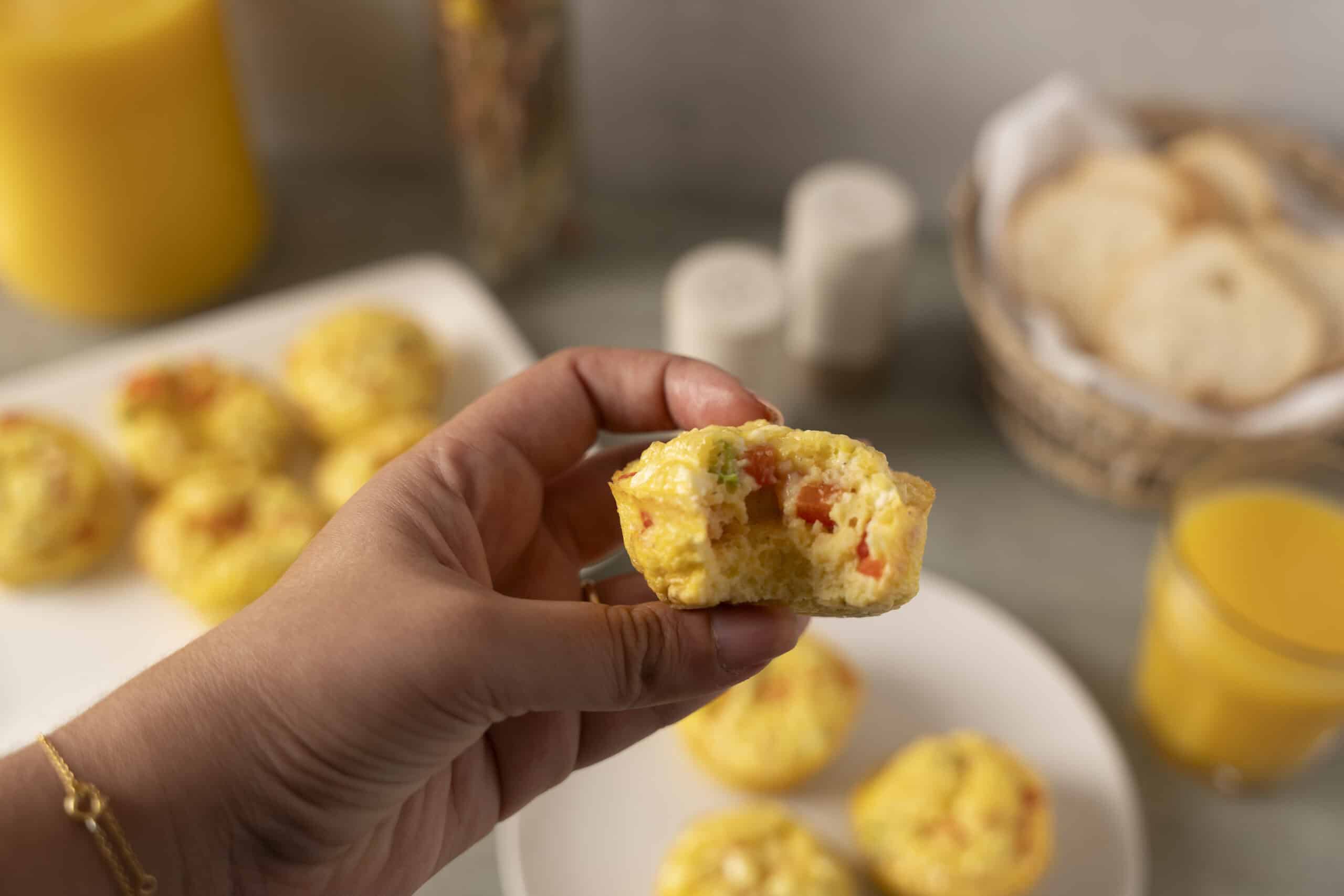 Crispy breakfast egg muffins with vegetables and cheese, close-up of hand holding a muffin with a bite taken out, healthy homemade egg muffins recipe for breakfast or brunch.