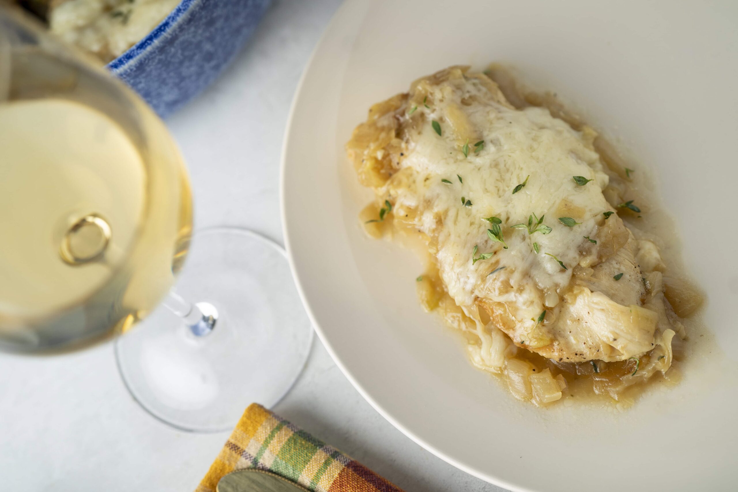Butter chicken casserole with melted cheese and fresh herbs served on a white plate, glass of white wine, colorful napkin, culinary dish, comfort food, easy dinner recipe, cheesy baked chicken, homemade chicken casserole, hearty chicken dish, savory comfort food.