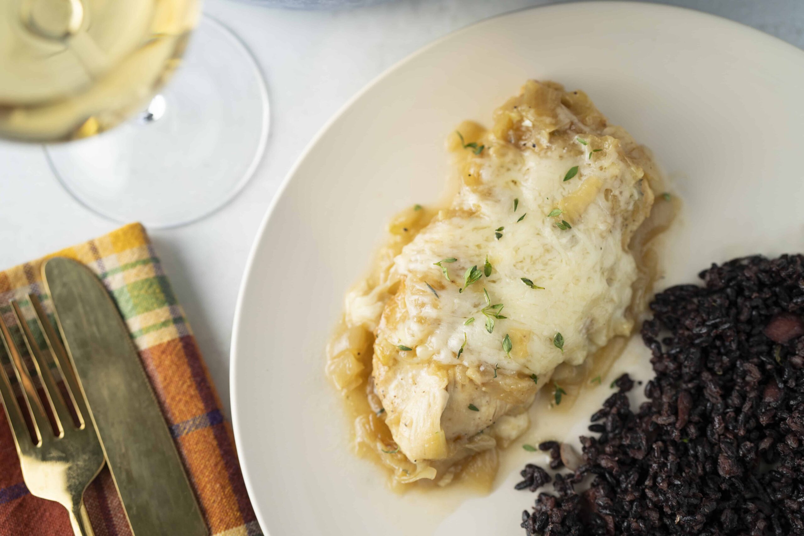 Creamy chicken and mashed potatoes topped with herbs served alongside black rice on a white plate. Perfect comfort food pairing with a glass of white wine.