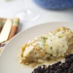 Creamy chicken pot pie with sautéed onions and herbs served with a side of wild rice on a white plate. Perfect comfort food recipe, ideal for family dinners and easy to prepare at home.