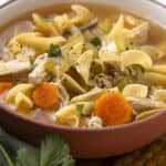 Warm homemade chicken noodle soup with vegetables, shredded chicken, carrots, celery, and herbs in a cozy bowl, perfect for a comforting meal.