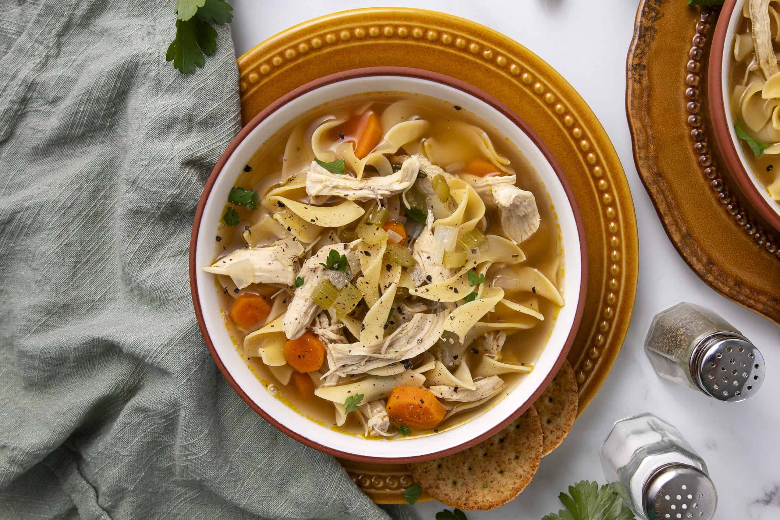 Creamy chicken noodle soup with vegetables in a white bowl, garnished with herbs on a rustic table setting.