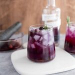 Sweet purple berry infused water with ice, garnished with rosemary, served in a clear glass. Refreshing and healthy beverage ideal for summer.