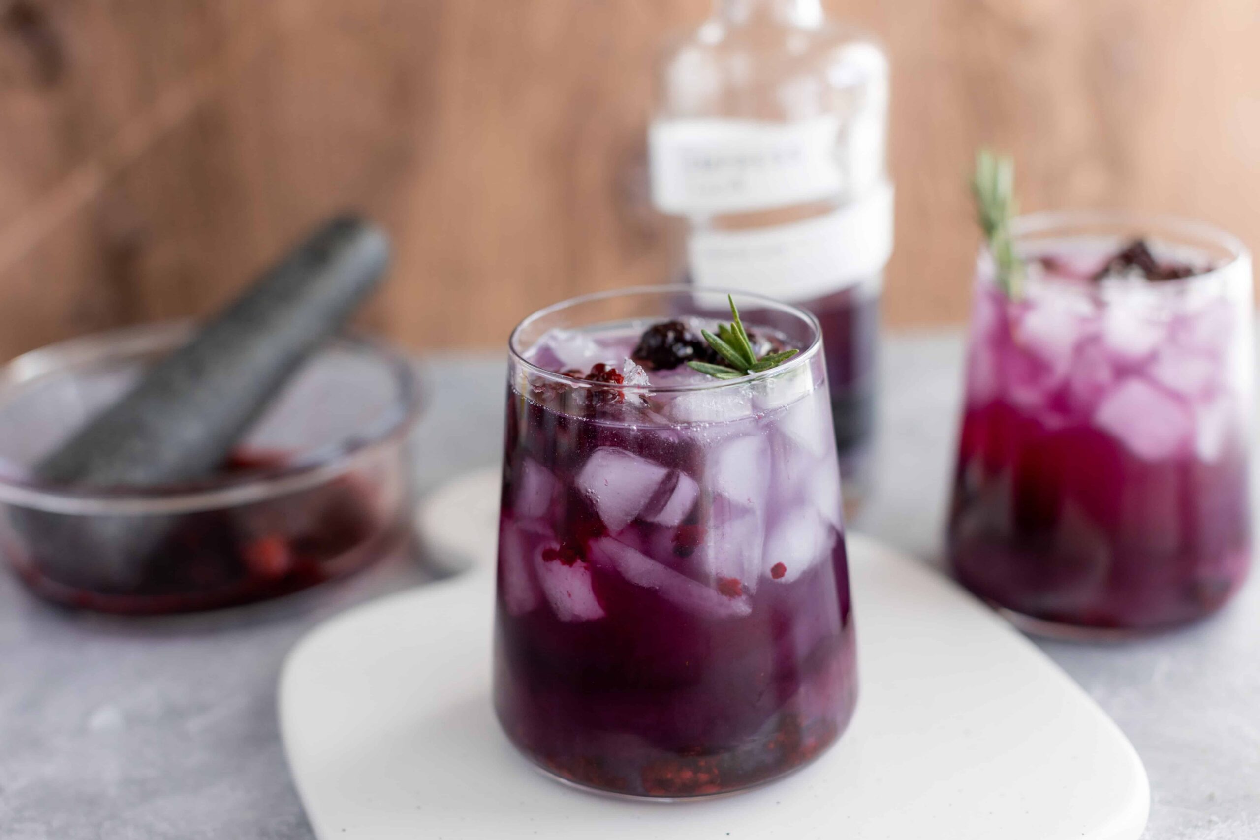 Fresh berry-infused purple cocktail with ice cubes and a sprig of rosemary, served in a clear glass. Perfect for summer drinks and berry recipes.