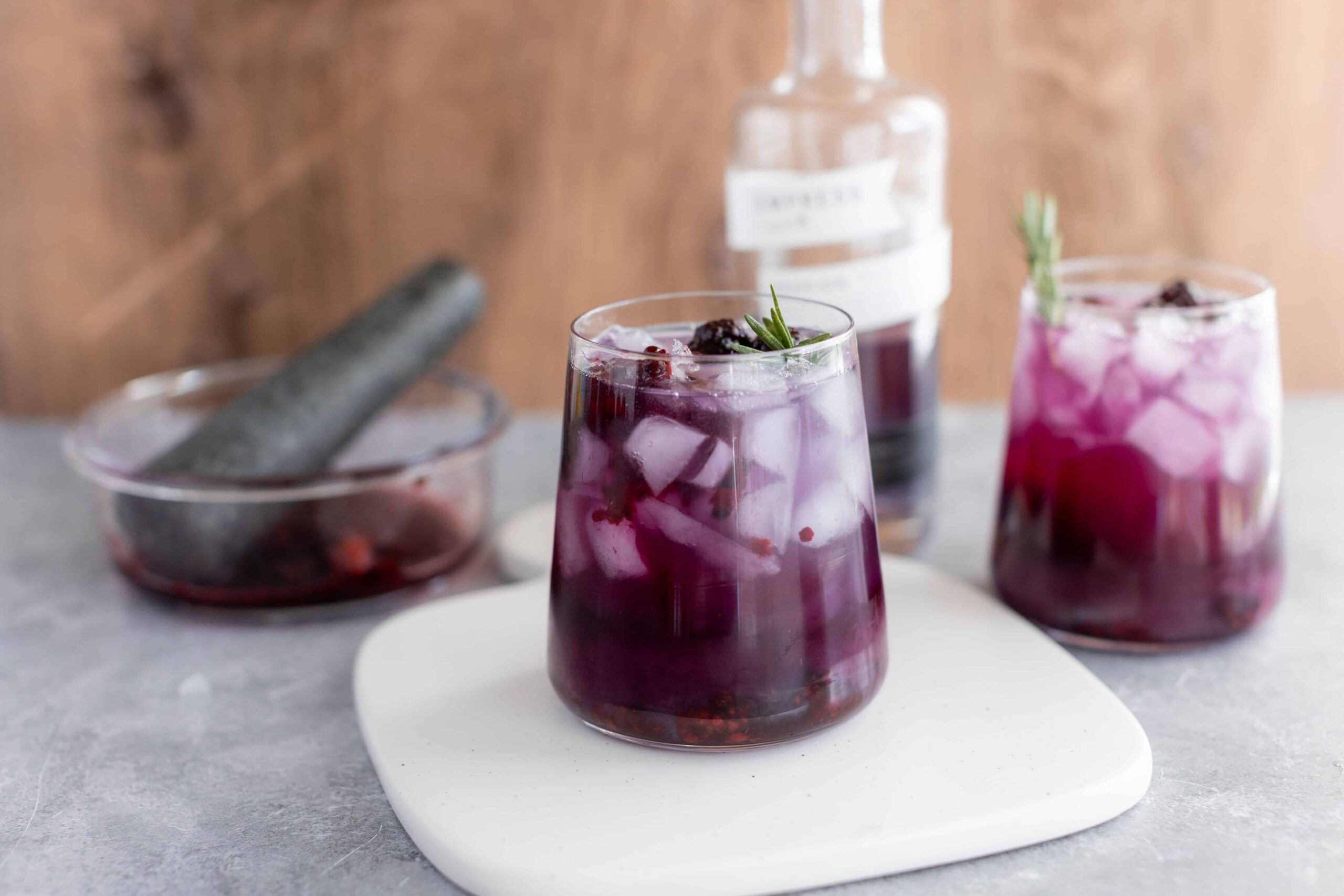 Sweet purple berry infused water with ice, garnished with rosemary, served in a clear glass. Refreshing and healthy beverage ideal for summer.