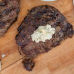 Juicy grilled steak topped with a dollop of blue cheese butter on a wooden cutting board. Perfect for a hearty meal, indoor grilling, and special occasions.