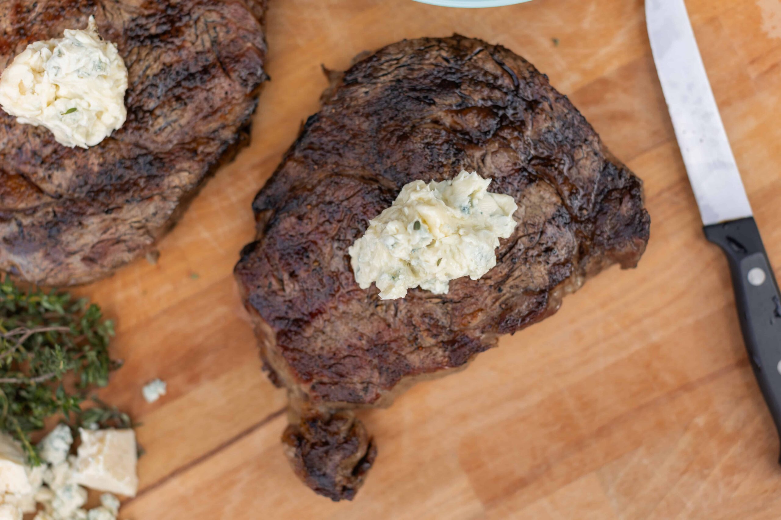 Juicy grilled steak topped with a dollop of blue cheese butter on a wooden cutting board. Perfect for a hearty meal, indoor grilling, and special occasions.