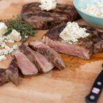 Juicy grilled steak topped with creamy blue cheese crumbles, sliced and served on a wooden cutting board with fresh herbs and a side of blue cheese dressing. Perfect for steak lovers and cheese enthusiasts.