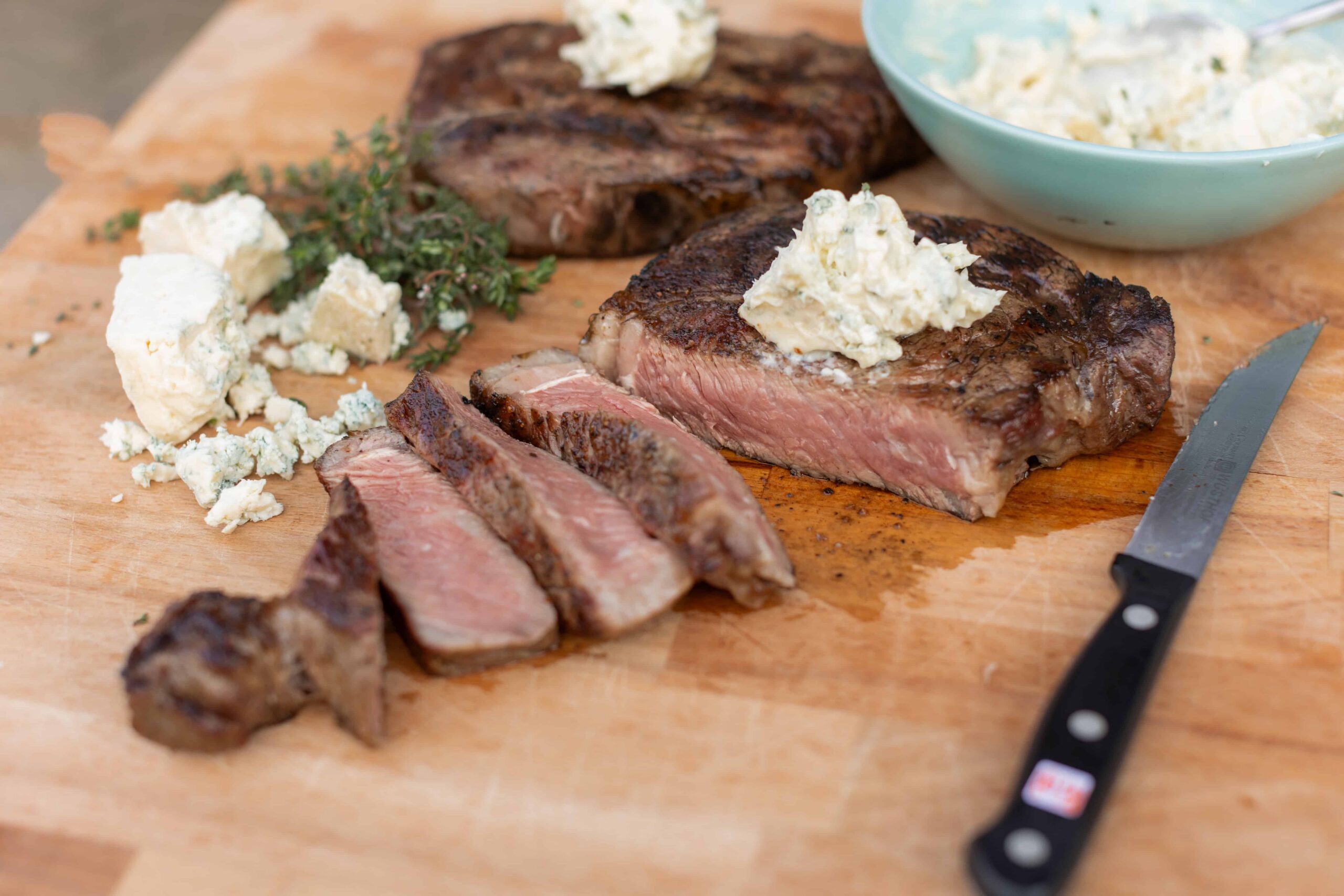 Juicy grilled steak topped with creamy blue cheese crumbles, sliced and served on a wooden cutting board with fresh herbs and a side of blue cheese dressing. Perfect for steak lovers and cheese enthusiasts.