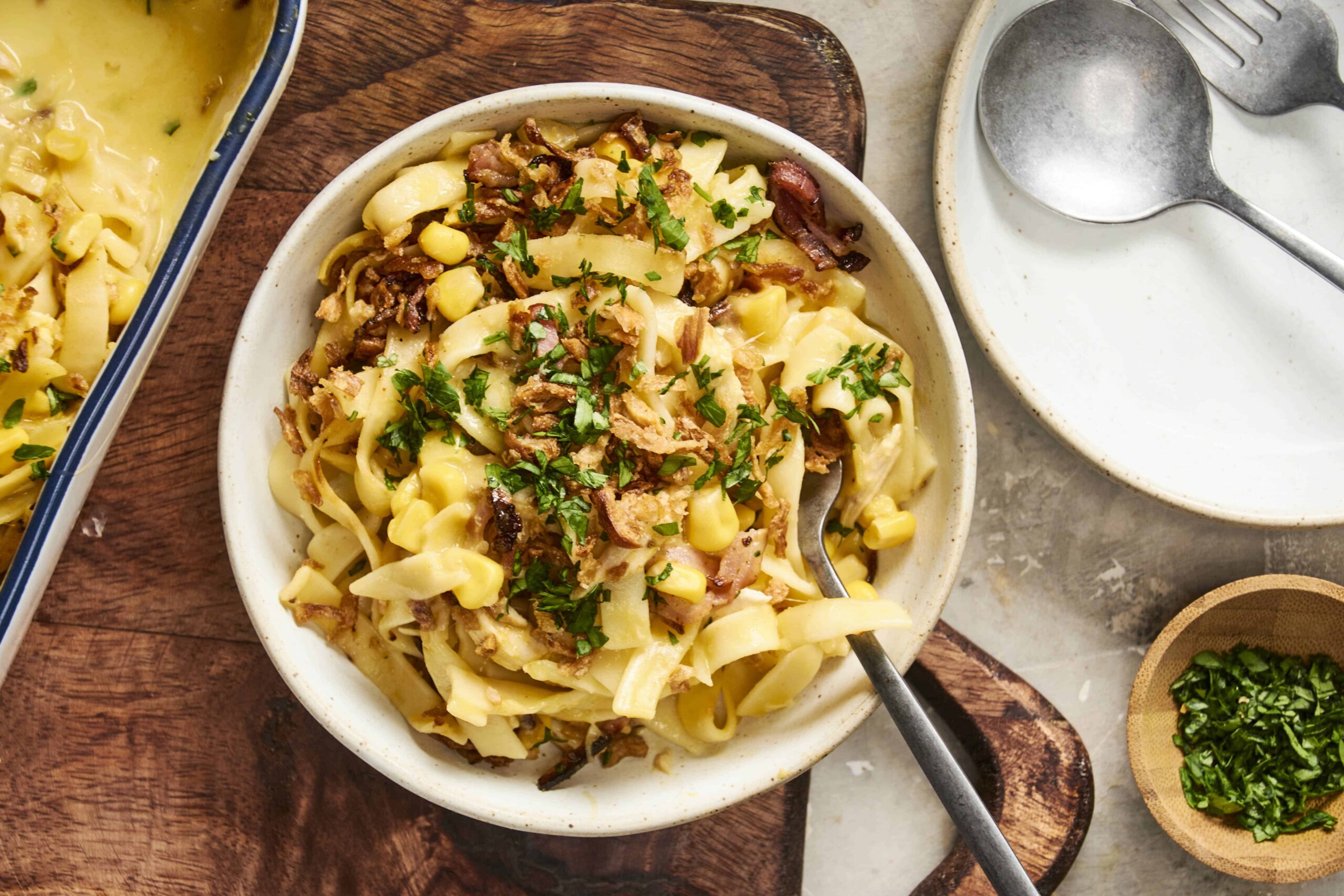 Creamy pasta casserole with bacon, corn, and fresh herbs in a white bowl, served with a spoon; a delicious comfort food recipe from Hey Recipe.