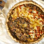Golden-brown homemade savory beef and vegetable pie with melted cheese and fresh diced red peppers on top, served on parchment paper with a side of fresh basil leaves, perfect for a comforting meal.