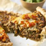 Savory homemade meat and vegetable pie with a crispy crust and melted cheese topping, perfect for family dinners or comfort food, on a rustic surface with a fork for serving.