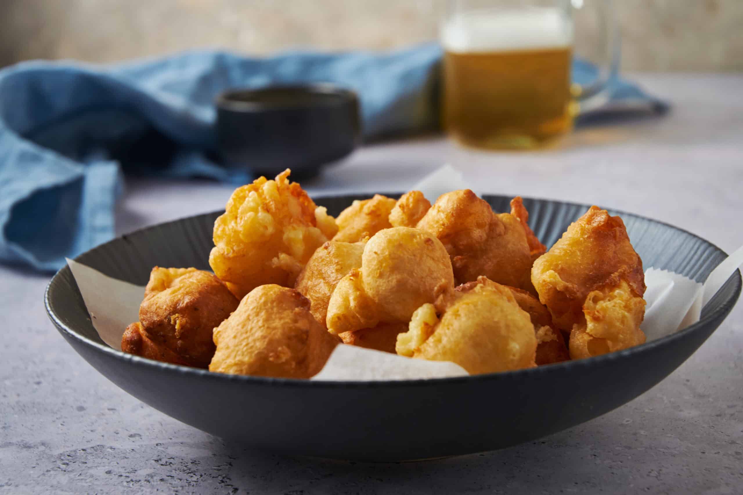 Crispy golden battered fried chicken pieces served in a black bowl on a textured surface, with a side of beer and dipping sauce in the background, perfect for comfort food and snack recipes.