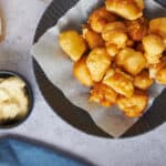 Crispy homemade fish nuggets served with creamy dipping sauce and tartar sauce on a black plate, perfect for snacks or fish burger recipes.