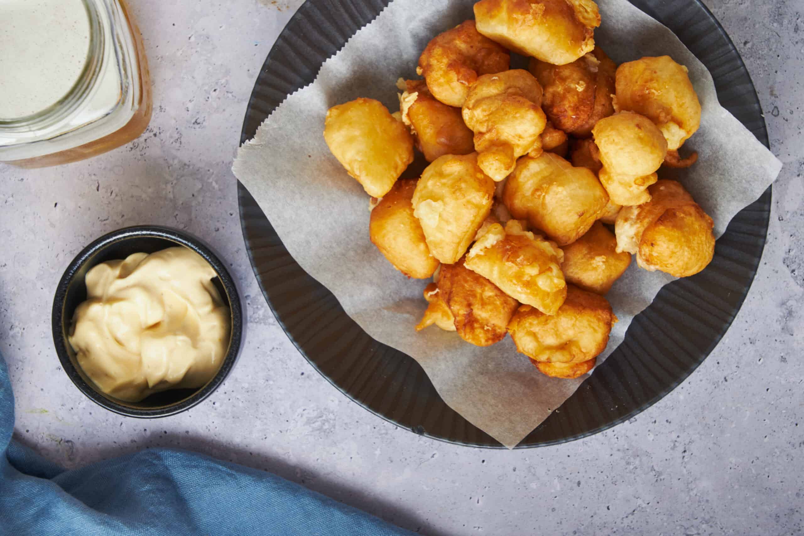Crispy homemade fish nuggets served with creamy dipping sauce and tartar sauce on a black plate, perfect for snacks or fish burger recipes.