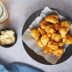 Crispy battered fish nuggets served on a black plate with parchment paper, accompanied by tartar sauce and creamy mayonnaise, ideal for crispy fish recipes and seafood snacks.