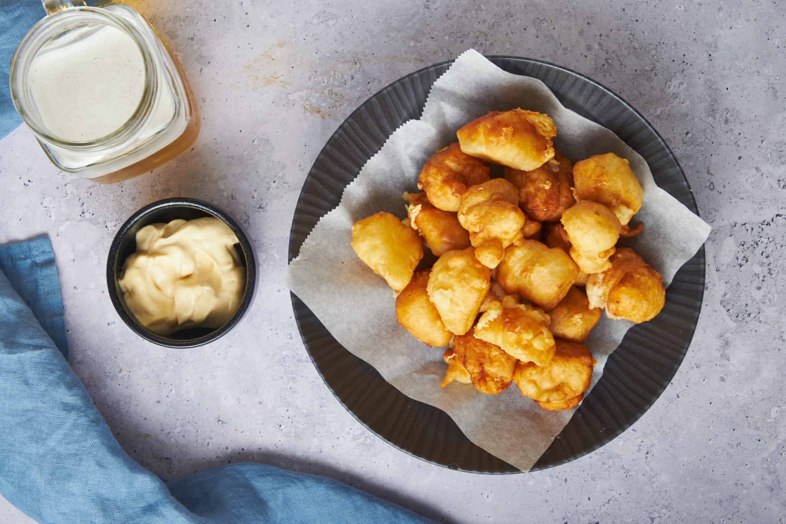 Crispy battered fish nuggets served on a black plate with parchment paper, accompanied by tartar sauce and creamy mayonnaise, ideal for crispy fish recipes and seafood snacks.