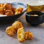Golden crispy fried cauliflower bites served with dipping sauces on a textured surface. Perfect for snacks or appetizers, showcasing healthy vegetarian fried food options.