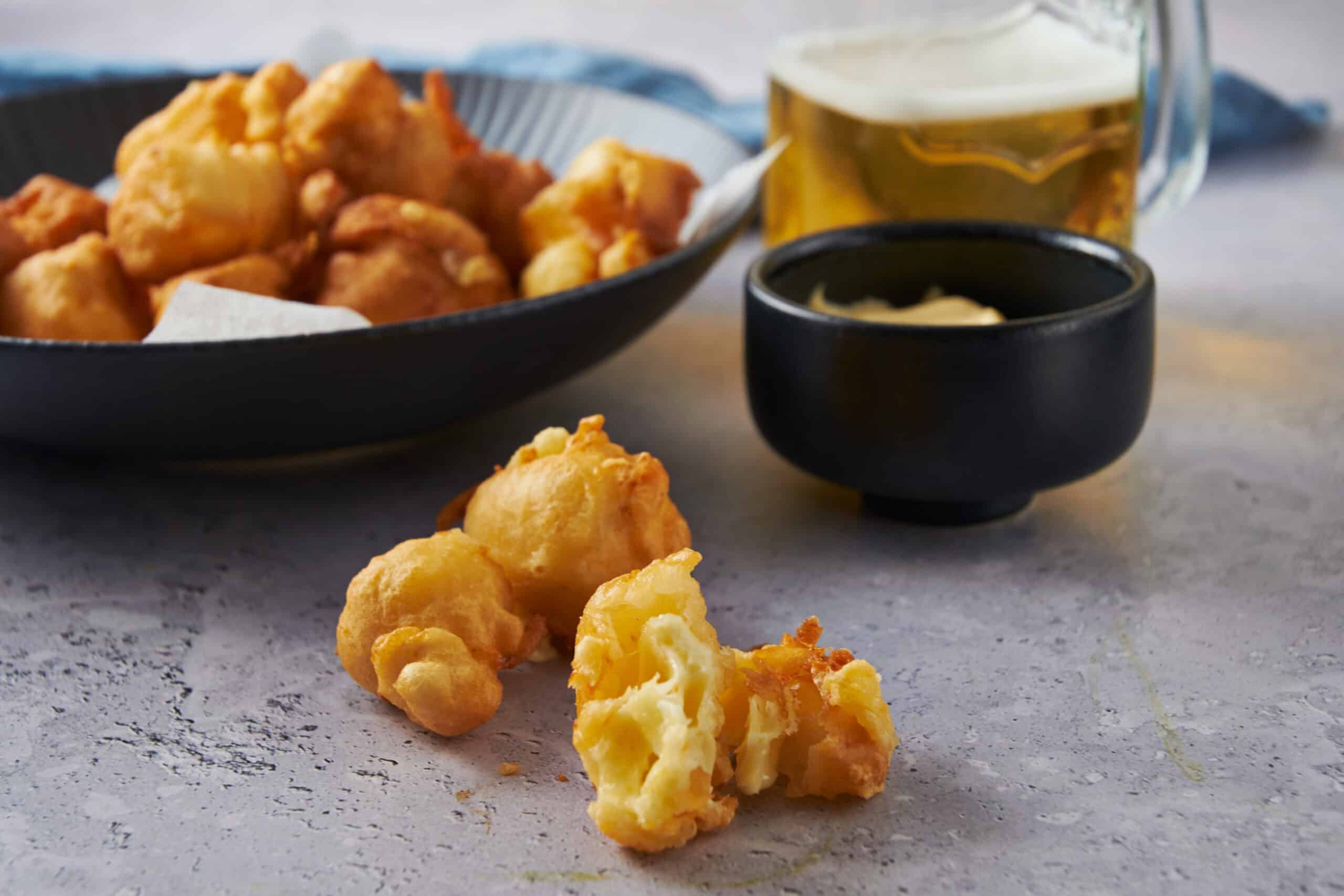 Golden crispy fried cauliflower bites served with dipping sauces on a textured surface. Perfect for snacks or appetizers, showcasing healthy vegetarian fried food options.