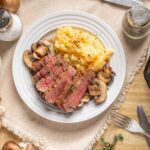 Succulent beef steak with mushroom sauce and creamy mashed potatoes served on a white plate for a hearty meal. Perfect comfort food for dinner or special occasions.