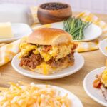 Scrambled egg breakfast sliders with ground beef and cheese on a white plate, cozy breakfast scene, hearty breakfast sandwich with eggs and meat, delicious brunch idea for morning meal, Hey Recipe.