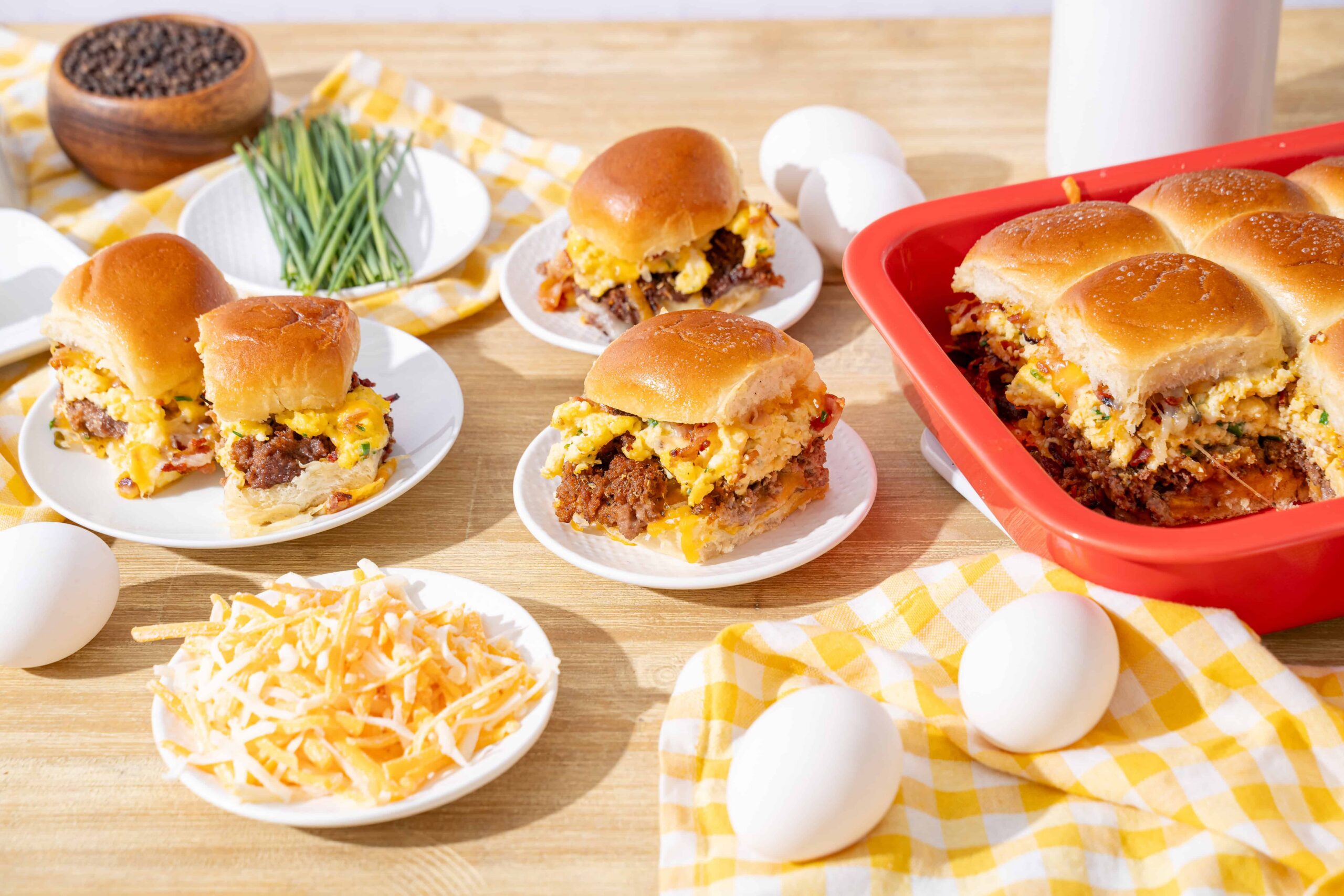 Savory breakfast casserole with eggs, sausage, cheese, and bread baked in a red dish, served with fresh eggs, shredded cheese, and chives on a wooden table. Perfect for brunch or quick family breakfast.
