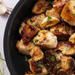 Juicy, grilled chicken pieces garnished with herbs in a black skillet, showcasing a delicious and savory dish perfect for dinner or lunch.