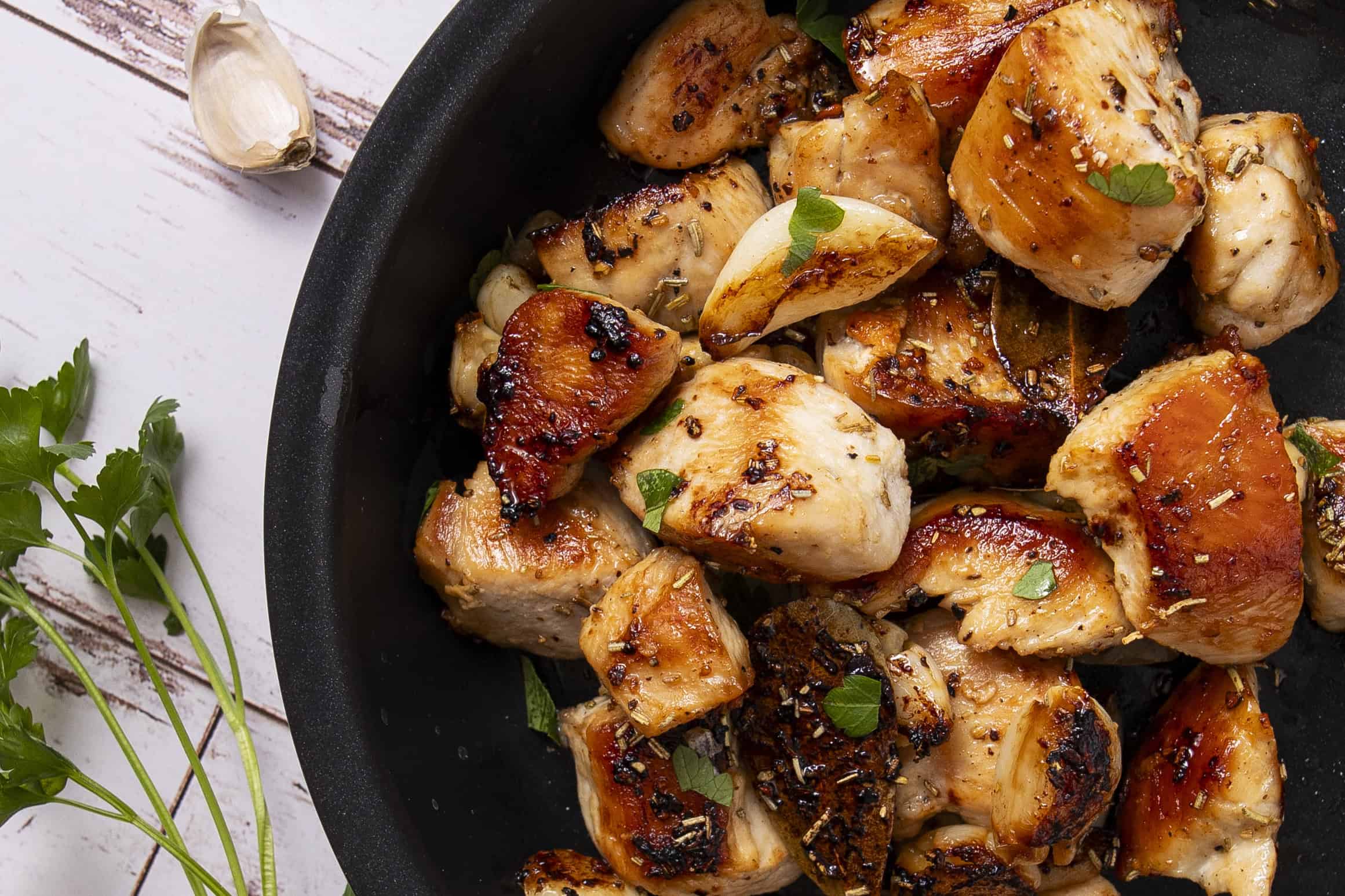 Juicy, grilled chicken pieces garnished with herbs in a black skillet, showcasing a delicious and savory dish perfect for dinner or lunch.