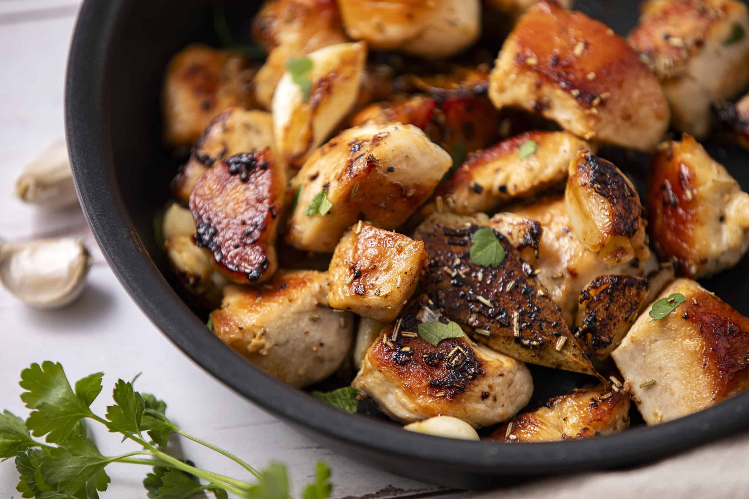 Juicy, flavorful roasted chicken breast pieces with crispy skin, garnished with fresh herbs, cooked to perfection in a black skillet for a delicious meal.