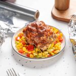 Savory meatloaf topped with rich gravy served on a bed of colorful cooked vegetables, with foil-wrapped portions in the background, perfect for a hearty homemade dinner.