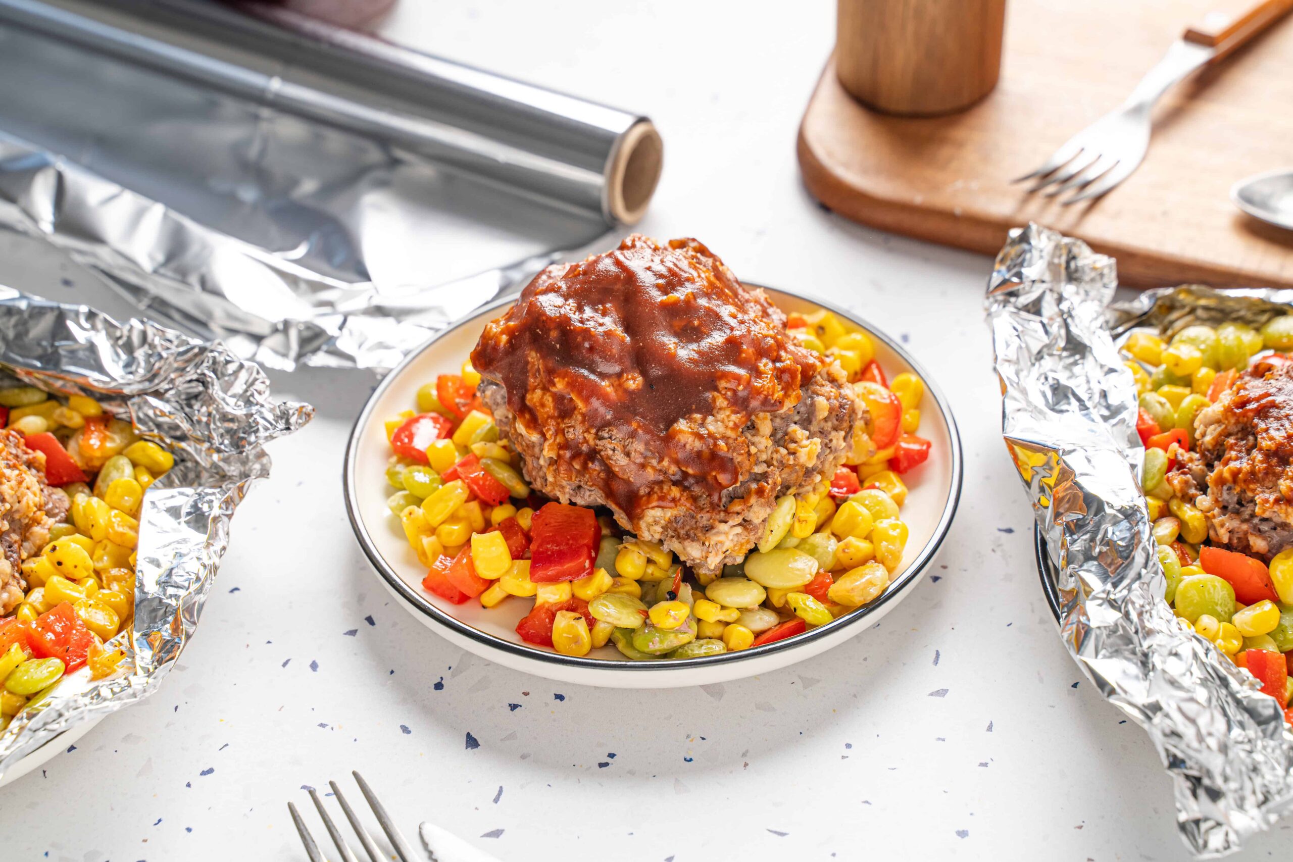 Savory meatloaf topped with rich gravy served on a bed of colorful cooked vegetables, with foil-wrapped portions in the background, perfect for a hearty homemade dinner.