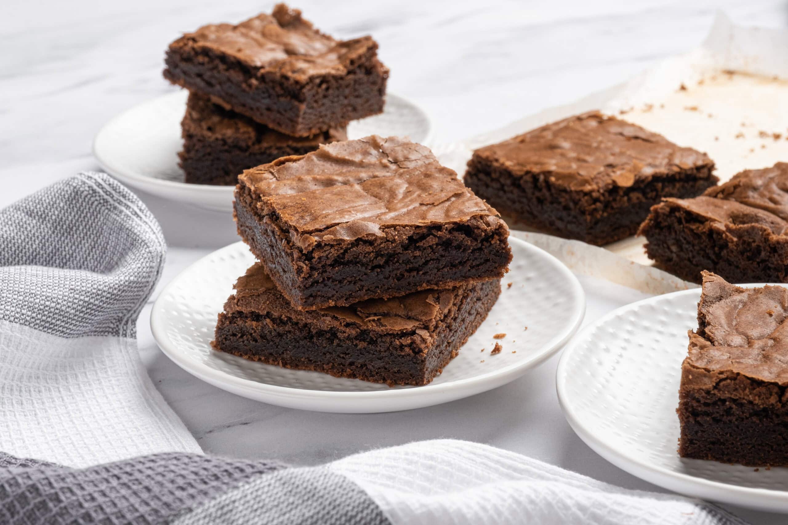 Rich, fudgy chocolate brownies on white plates with a marble background, perfect for dessert or snack, featuring classic homemade brownie recipes with melted chocolate and cocoa.